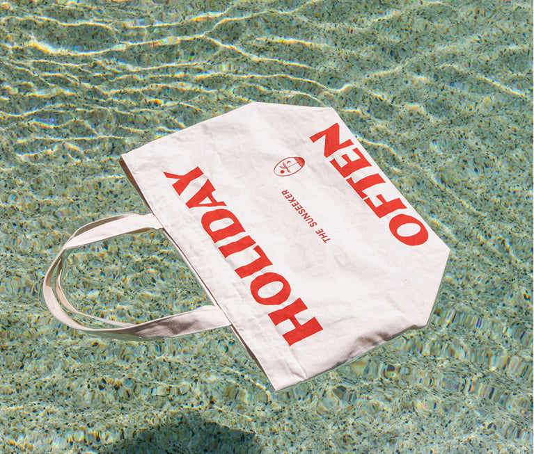 A Worktones custom Market Bag with red Screen Printing that reads "Holiday Often" and "The Sunseeker" floats on top of pool water.